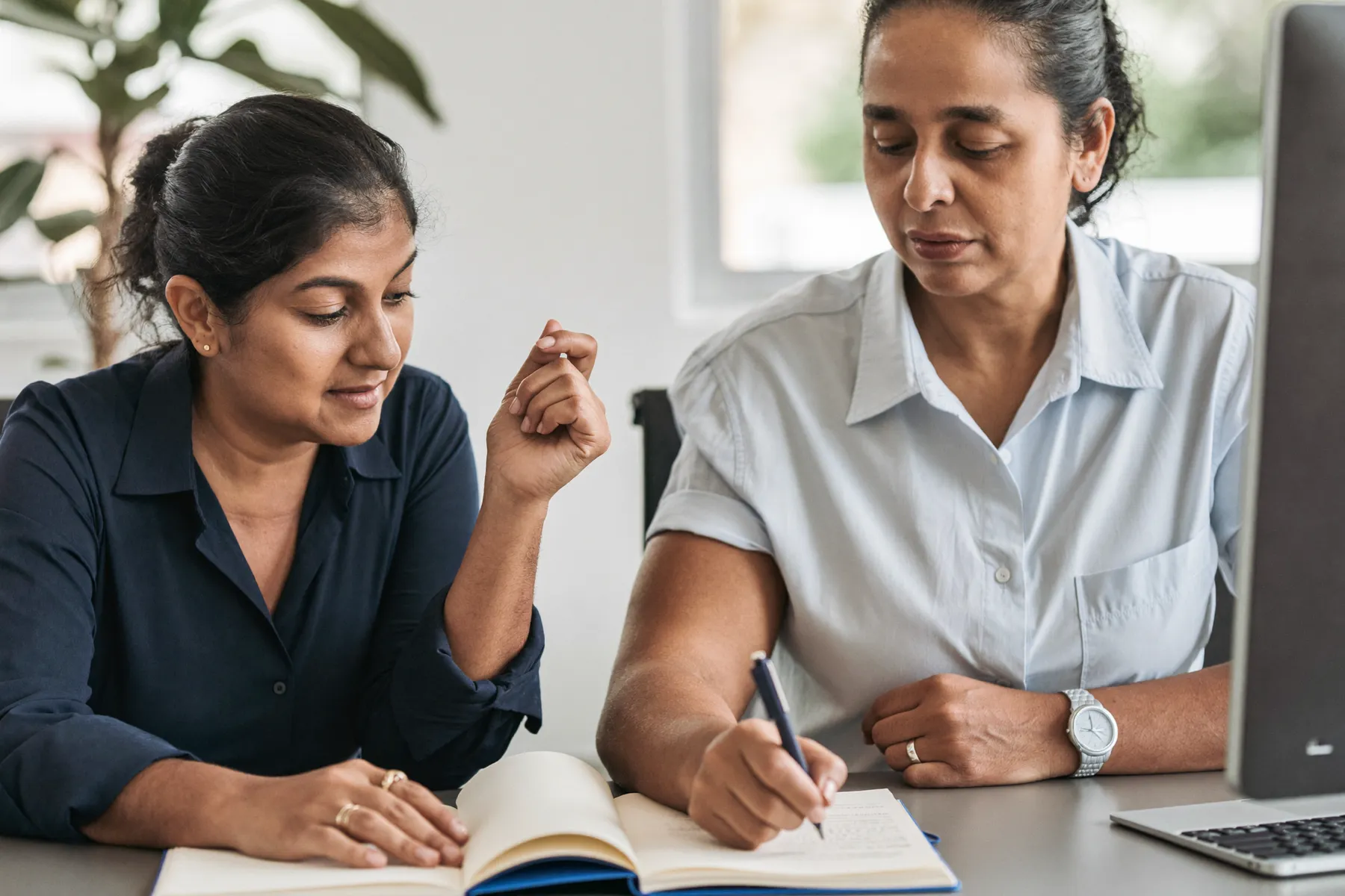 An experienced manager coaching a newer colleague over an open notebook