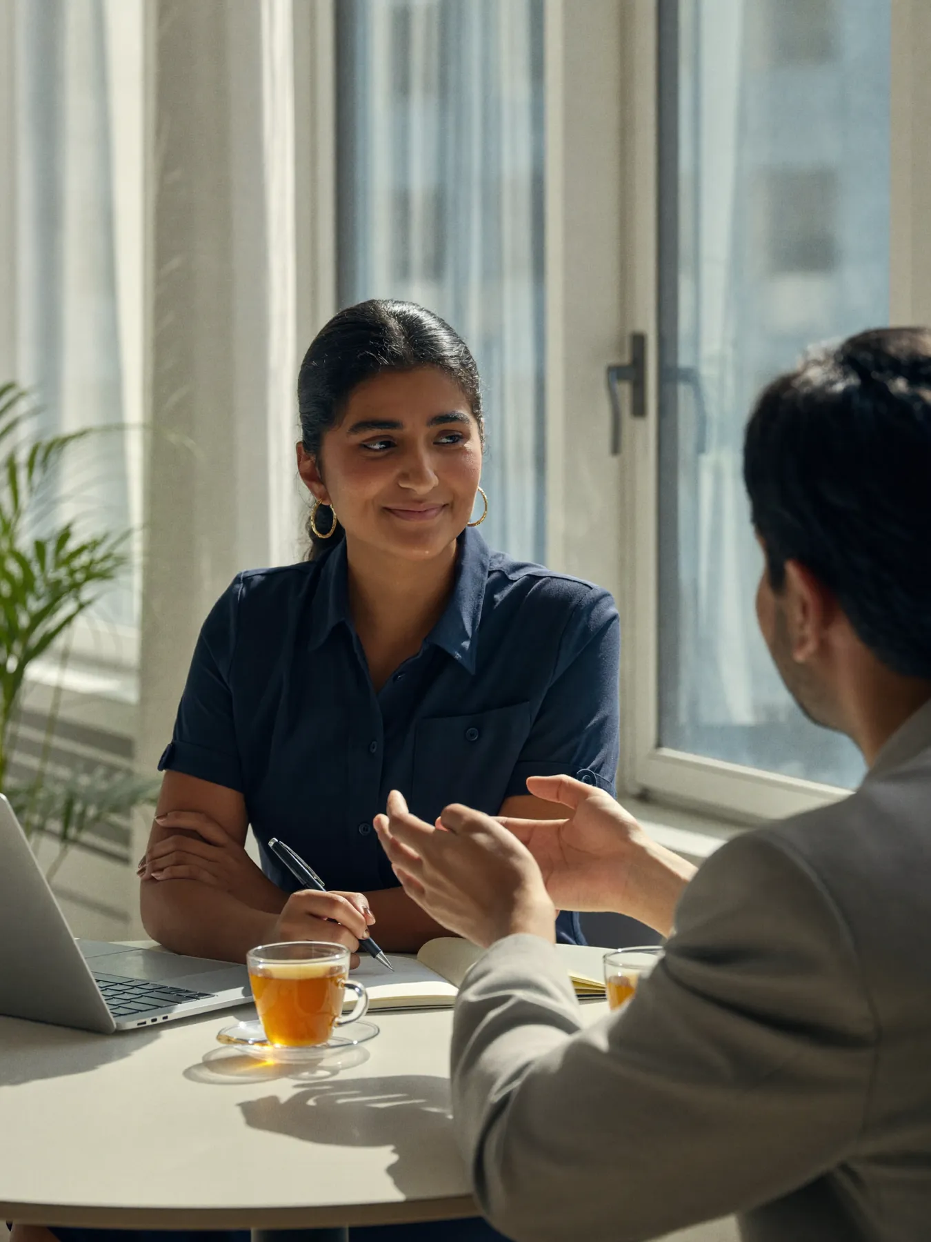Two colleagues in a calm one-to-one conversation over chai by a sunlit window