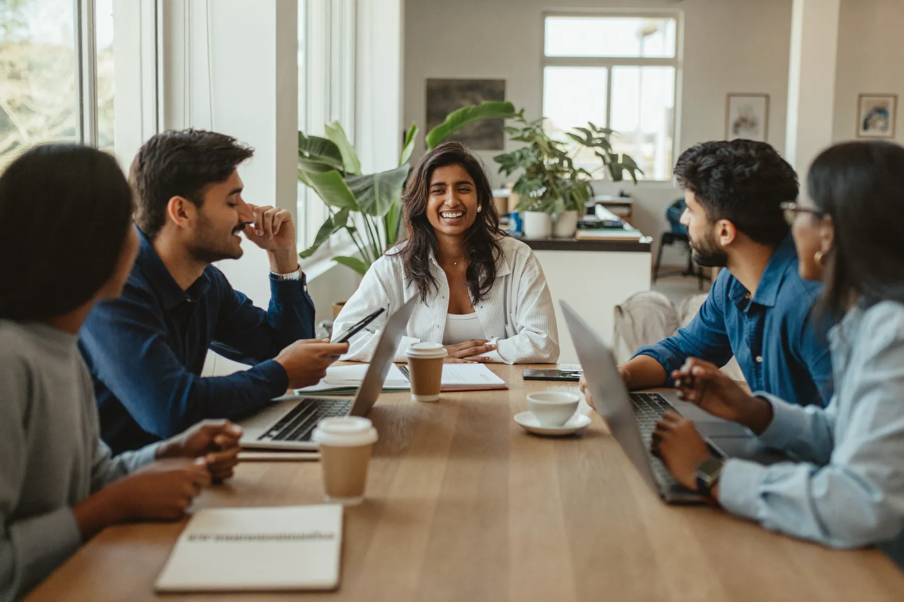 A small team laughing together around a long table in a light-filled office